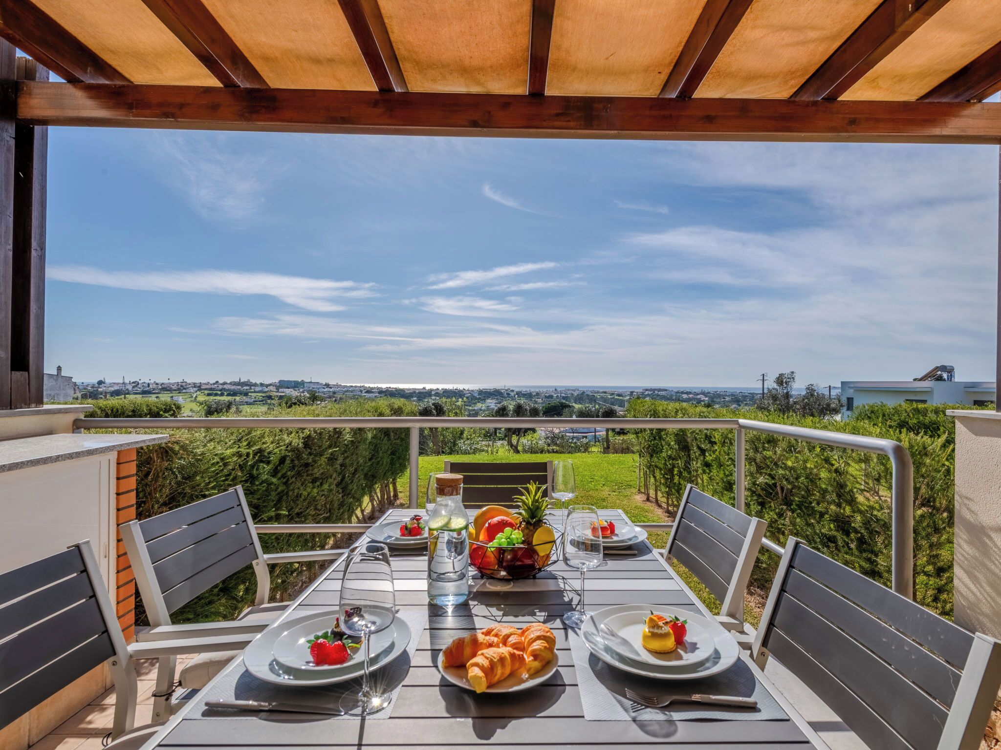 An outdoor dining area with a table set for two, a view of the countryside, and a pergola overhead.