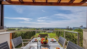 Een buiten eethoek met een tafel voor twee personen, uitzicht op het landschap en een pergola erboven.