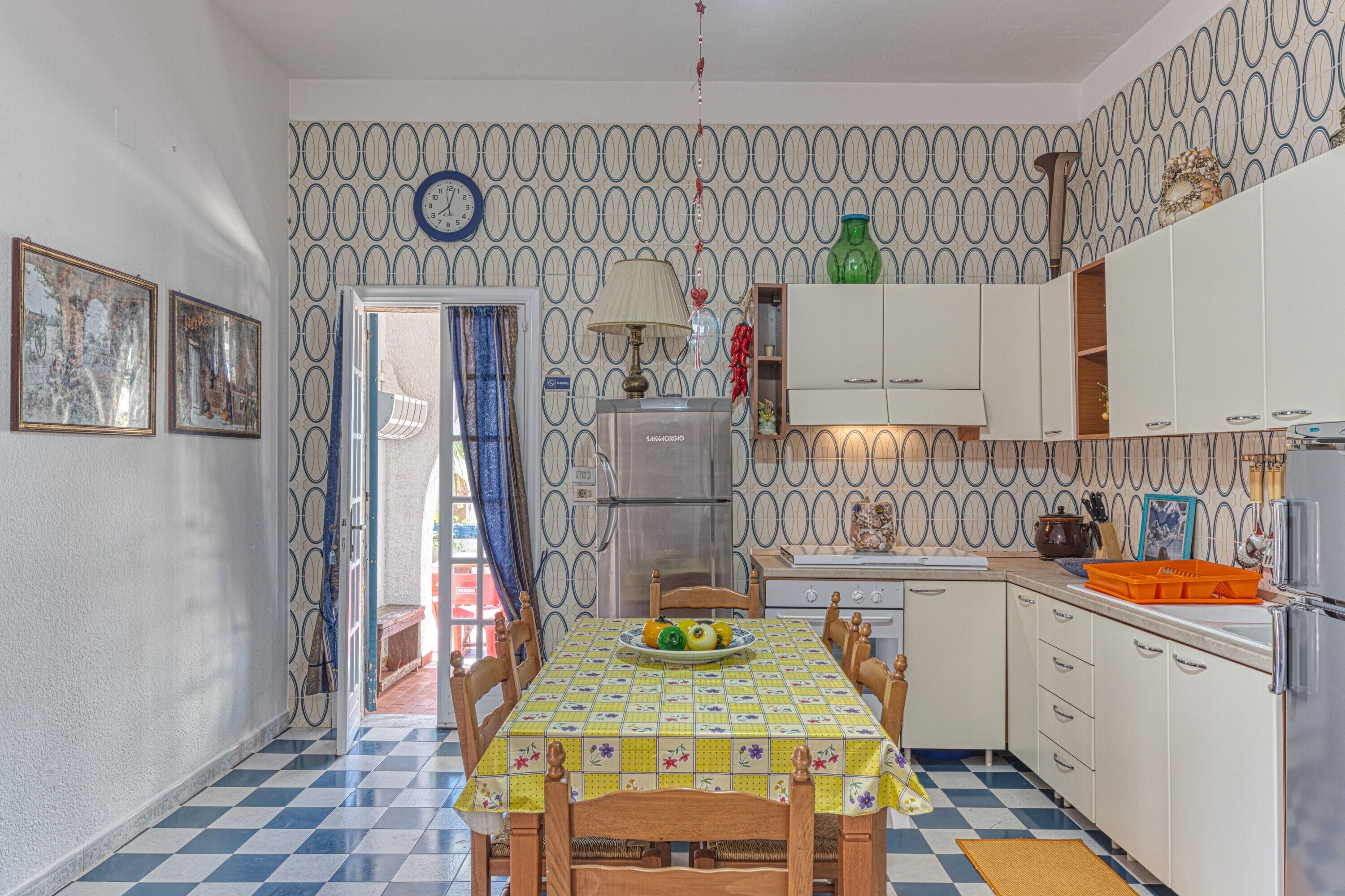 Eine Küche mit Schachbrettboden, einem Esstisch mit Stühlen, einem Kühlschrank und einer Wand mit Muster.