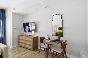 A hotel room with a wooden dresser, a round dining table with chairs, a television, a mirror, and a potted plant. - Studio condo at Luau in Sandestin Golf & Beach Resort (Miramar Beach)