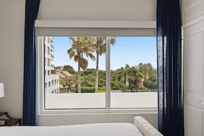 A hotel room with a large window, a bed, a nightstand, and a view of palm trees and buildings. - Studio condo at Luau in Sandestin Golf & Beach Resort (Miramar Beach)