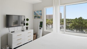 Un dormitorio con un ventanal grande, un televisor de pantalla plana, un aparador blanco y un cuadro en la pared.