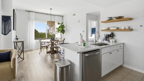 Una cocina moderna con una isla central, armarios blancos y un comedor con mesa y sillas.