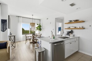 Una cocina moderna con una isla central, armarios blancos y un comedor con mesa y sillas.