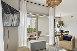 Una sala de estar con televisor, sofá, mesa de comedor con sillas y balcón con vista a edificios.