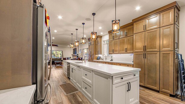 Une cuisine moderne dotée d’un îlot central, de meubles en bois, de luminaires suspendus et d’un réfrigérateur en acier inoxydable.