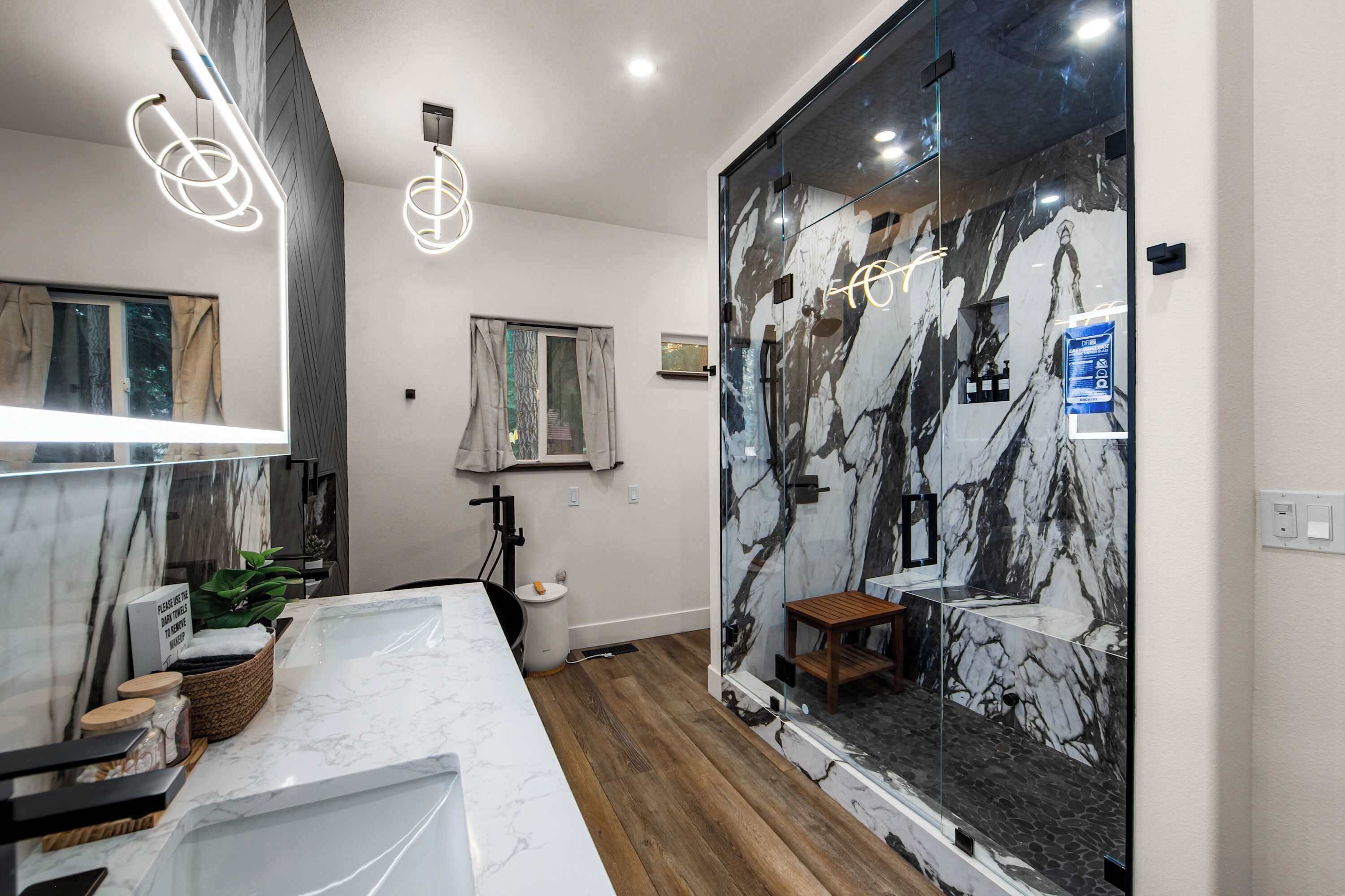 A modern bathroom with a marble vanity, a glass shower enclosure, and a wooden floor.