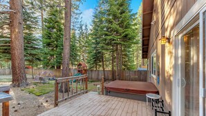 Une terrasse en bois avec un jacuzzi, un espace salon couvert et une vue sur une zone boisée.