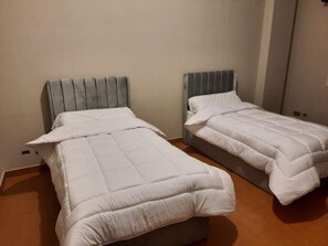 Two single beds with headboards, a wooden floor, and a plain wall. - 2BR Apt in Al Yassmin - Mynt Hospitality (Cairo)
