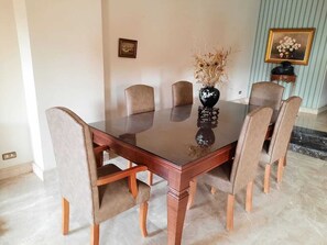 Mesa de jantar com seis cadeiras, vaso com plantas secas e quadro na parede.