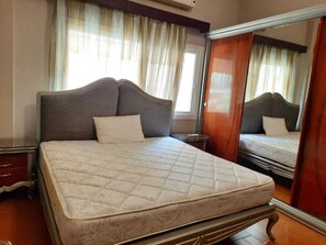 A bedroom with a bed, a dresser, a mirror, and curtains. - 2BR Apt in Al Yassmin - Mynt Hospitality (Cairo)