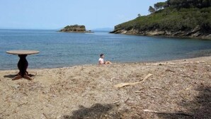 A beach with a table and a person sitting on the sand. - Villa Calamita apartment 1 (Capoliveri isola d'Elba)