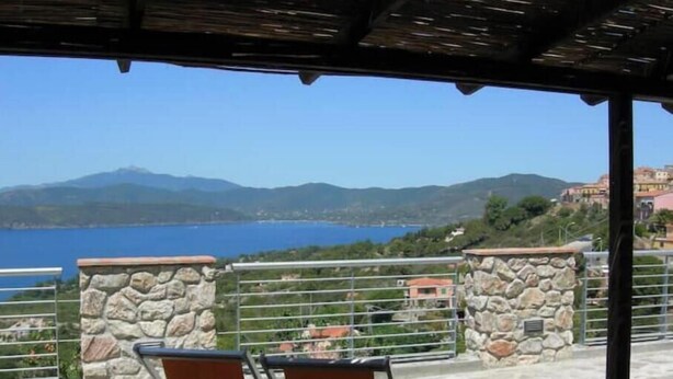 A covered outdoor seating area with stone walls and a view of a lake and mountains. - Villa Calamita apartment 1 (Capoliveri isola d'Elba)