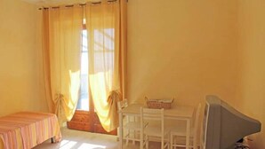 Quarto com uma cama, uma mesa com cadeiras, televisão e janela com cortinas.