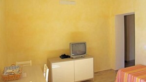 Quarto com televisão em um armário, mesa com cesta e cama com colcha listrada.