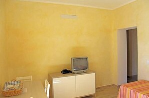 Ein Zimmer mit Fernseher auf einem Schrank, einem Tisch mit Korb und einem Bett mit gestreifter Bettdecke.