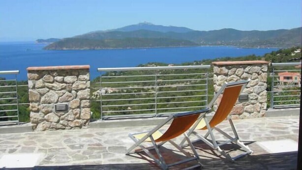 Uma área de estar ao ar livre com paredes de pedra e vista para o mar e montanhas.