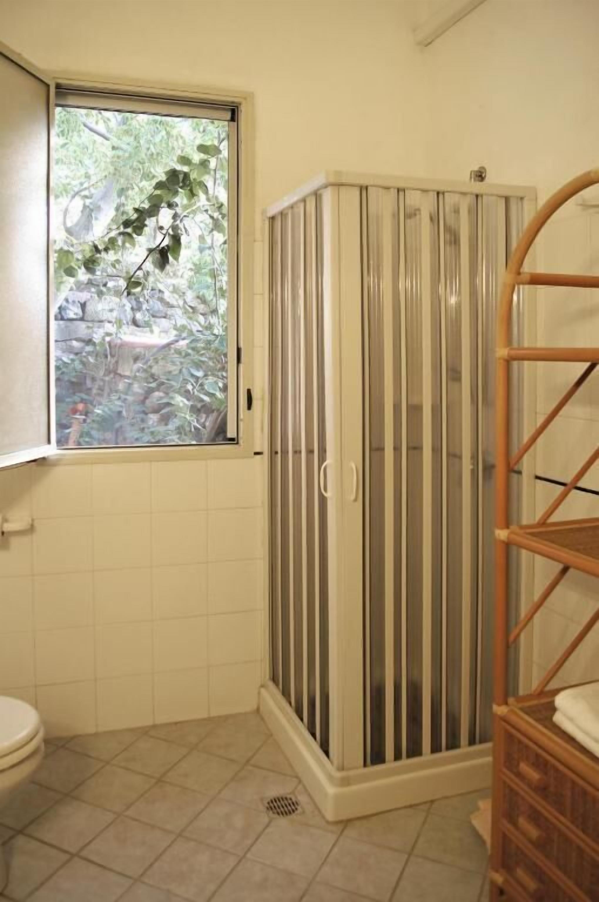 Une salle de bain avec douche, toilettes et une fenêtre donnant sur un espace verdoyant.