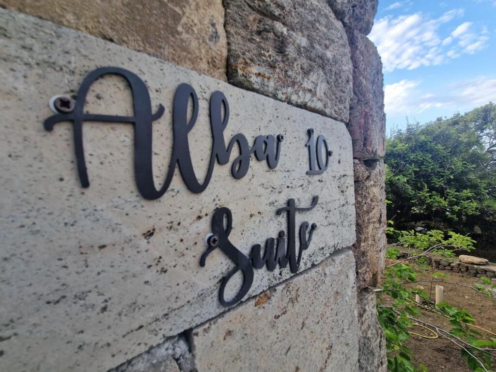 Une plaque portant l’inscription « Albar vers la suite » est fixée à un mur de pierre.