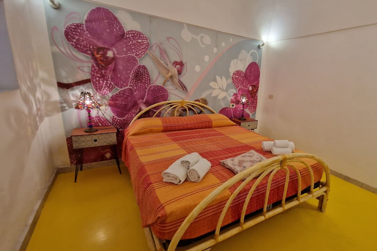A bed with a wooden frame, a yellow floor, and a wall with a floral mural.