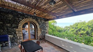 Un patio cubierto con paredes de piedra, una mesa, sillas y vistas al mar.