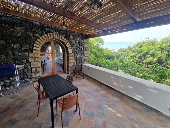 A covered patio with stone walls, a table, chairs, and a view of the sea.