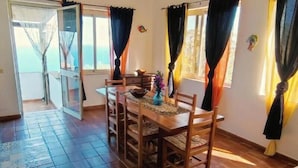 Un comedor con una mesa y sillas de madera, un florero con flores y vistas a través de una puerta abierta.