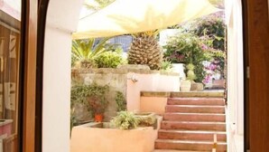 Un patio al aire libre con un banco de madera, una mesa y una escalera que lleva a una zona cubierta con plantas y un paraguas grande.