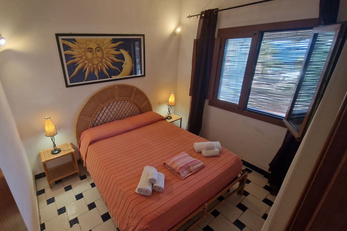 A bedroom with a bed, two bedside lamps, a wall-mounted artwork, and a window with blinds.