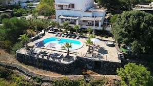 Una villa con piscina, rodeada de vegetación y un telón de fondo montañoso.