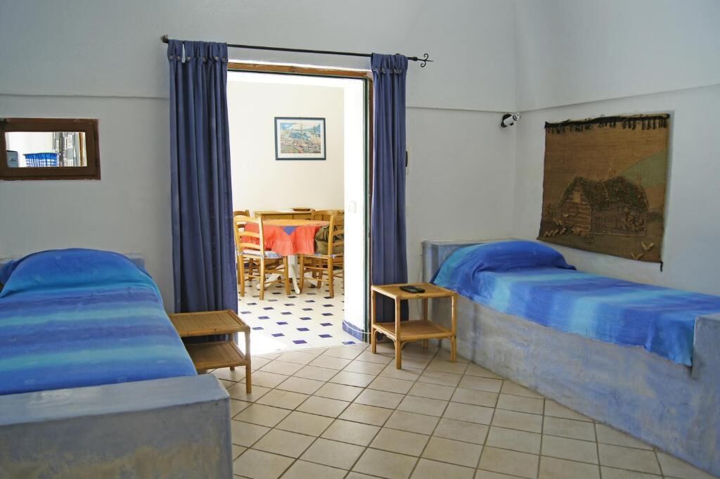 Una habitación con dos camas, una mesita, una silla y vista a un comedor por una puerta.