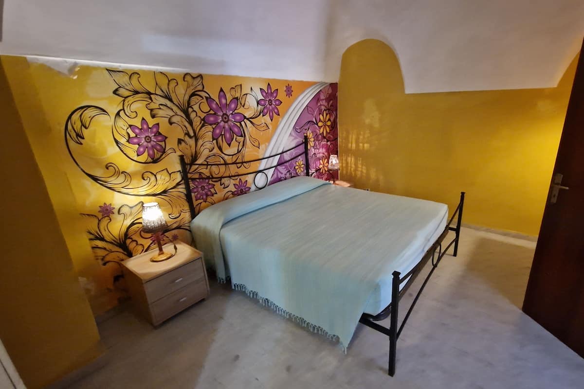 A bedroom with a bed, nightstand, lamp, and floral wallpaper.