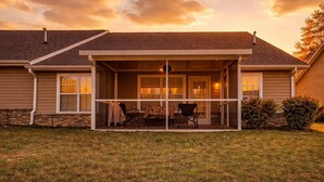Een huis met een overdekte patio, een stenen fundering en uitzicht op de oceaan bij zonsondergang.
