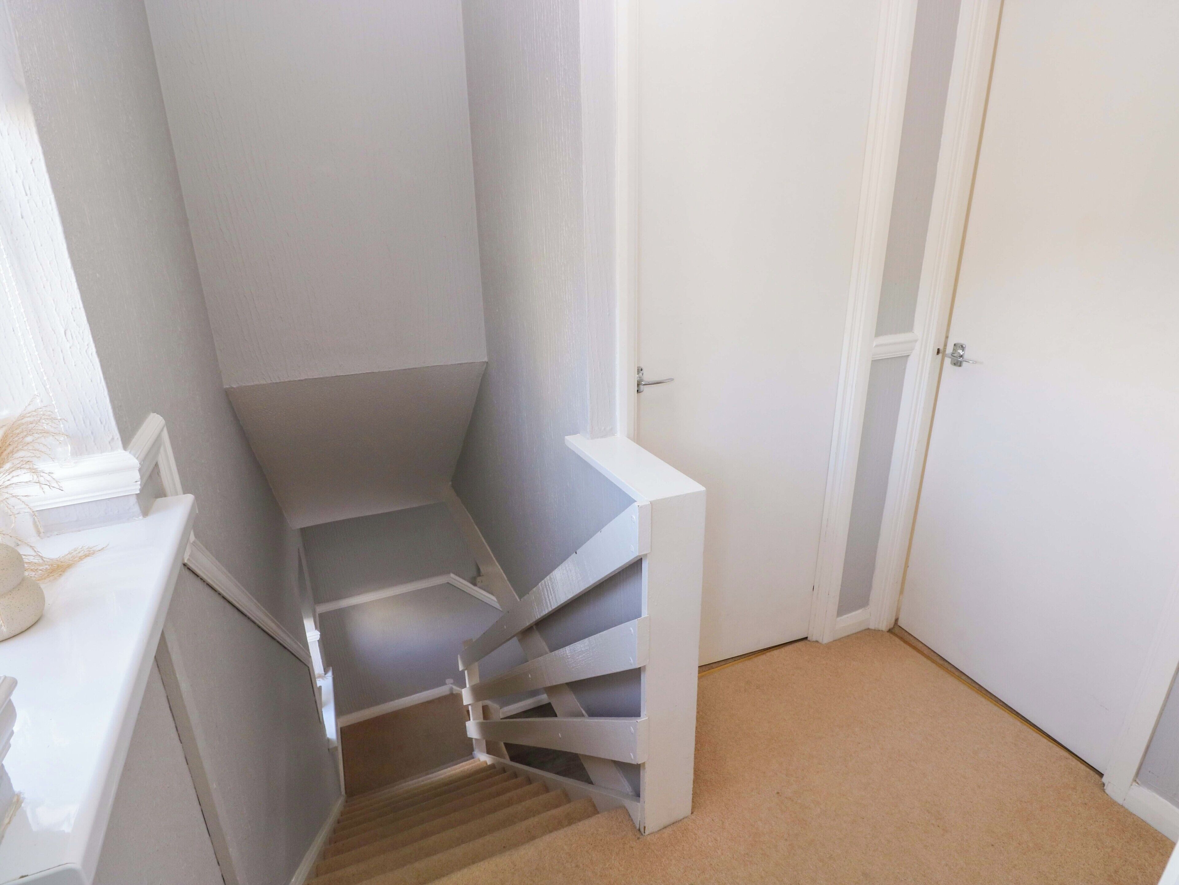 A narrow stairwell with a white door at the top and a white wall on one side.