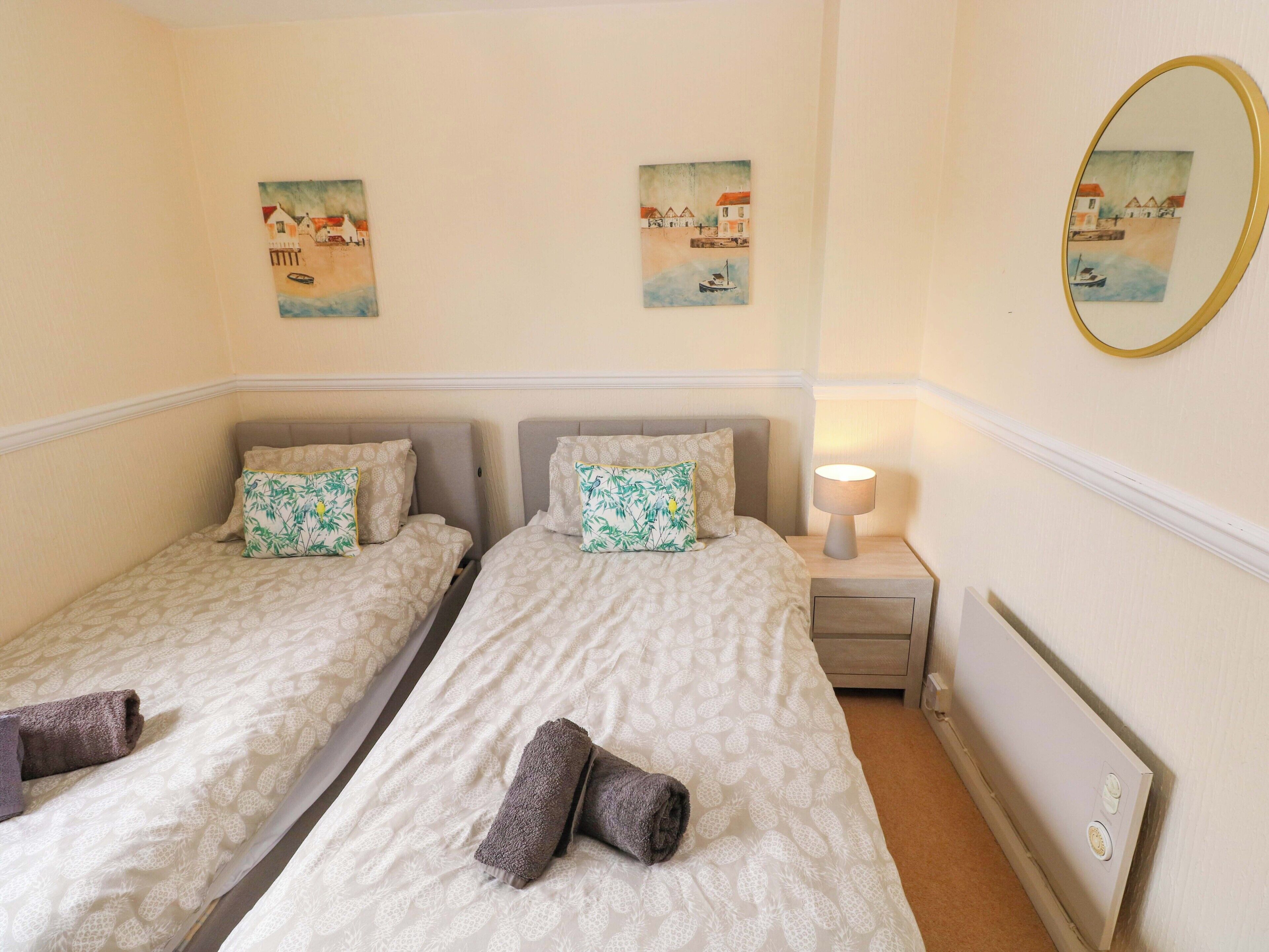 A hotel room with two beds, a nightstand with a lamp, and two wall-mounted paintings.