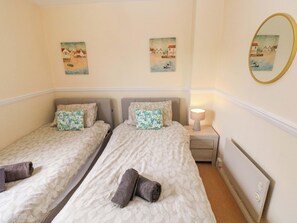 A hotel room with two beds, a nightstand with a lamp, and two wall-mounted paintings. - The Wool Pack (Tenby)