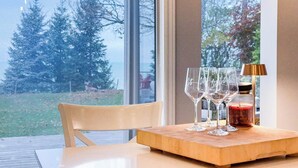 Una mesa con cuatro copas de vino, una vela, una lámpara y vistas de árboles a través de una ventana.