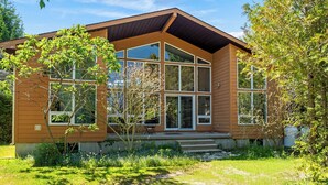 Una casa moderna con amplios ventanales, fachada de madera y un jardín cuidado.