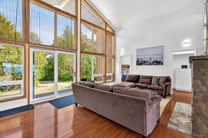 A spacious living room with large windows, a brown sofa, and a wooden floor.