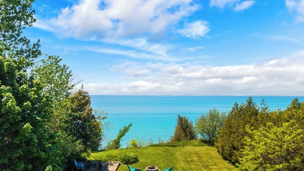 Un espacio al aire libre con césped y vistas al mar, una terraza de madera y sillas azules.