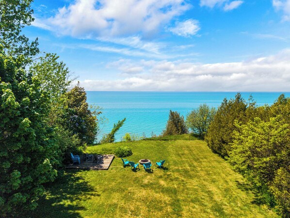 A grassy outdoor area with a view of the sea, a wooden deck, and blue chairs.