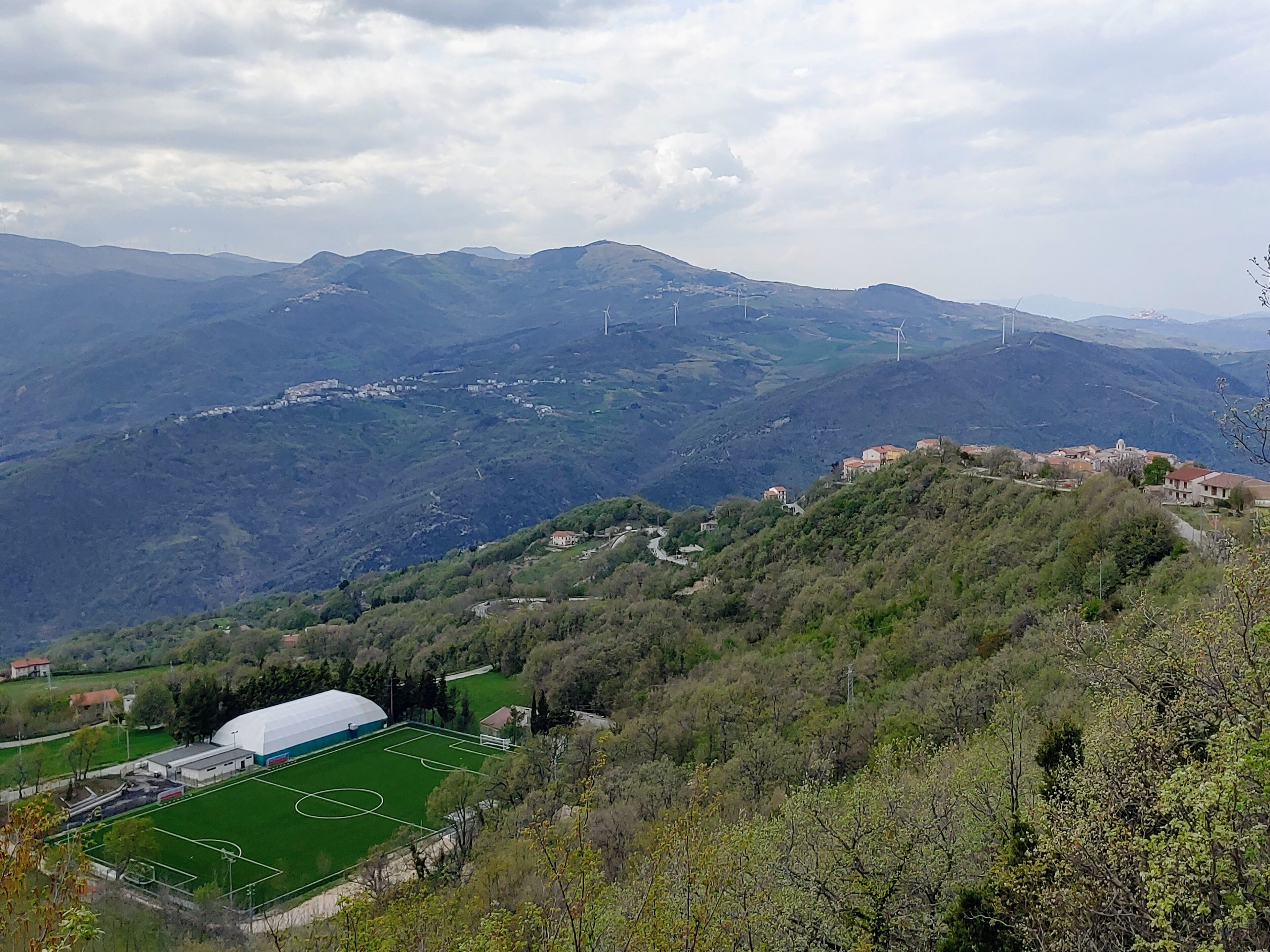Eine gebirgige Landschaft mit einem Fußballfeld, Gebäuden und Windkraftanlagen.