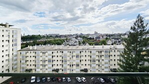 A high-rise building with multiple balconies, a parking lot with various cars, and a view of a cityscape with buildings and trees under a partly cloudy sky. - Pleasant, bright T3 on top floor (8), not overlooked, close to parks/services (Rennes)