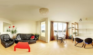 Ein Wohnzimmer mit einer schwarzen Ledersofa, einem roten Couchtisch und einem Essbereich mit weißem Tisch und Stühlen.