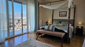 A four-poster bed with a bench, a view of the outdoors through a sliding door, and a small table with a lamp.