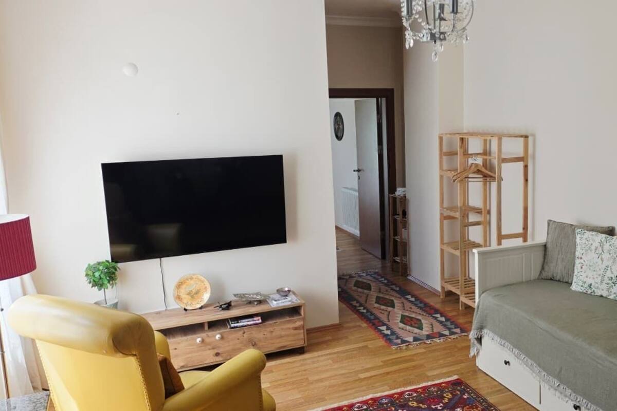 Un salon équipé d’un téléviseur à écran plat, d’un canapé, d’un fauteuil, d’une armoire en bois et d’un porte-manteau mural.