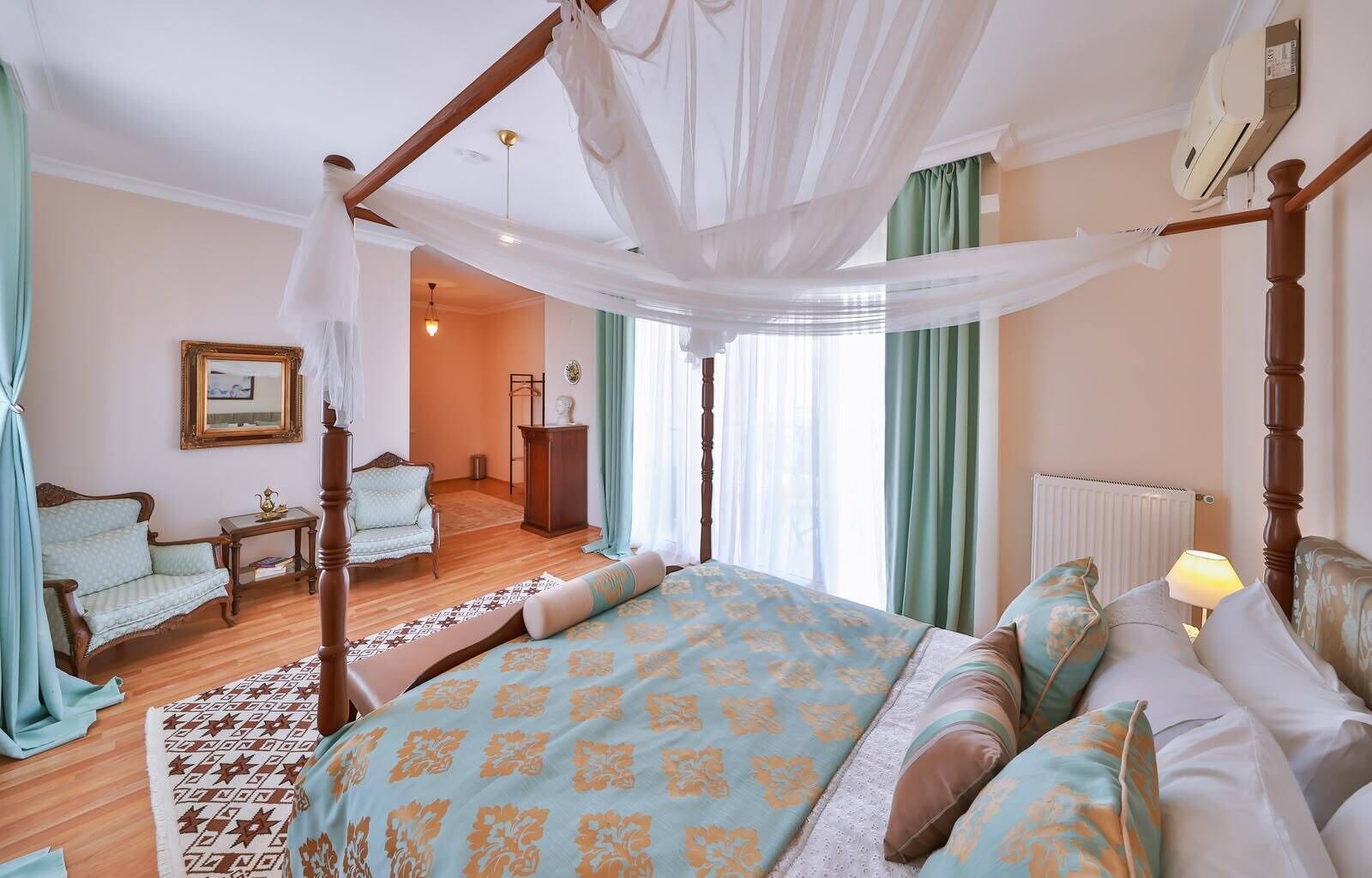 A bedroom with a four-poster bed, a sitting area with a chair and a table, and a view of the hallway.