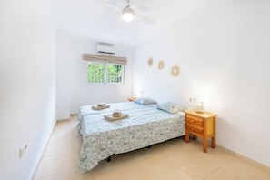 A bedroom with a bed, a nightstand, a ceiling fan, an air conditioner, and a window with a view. - Spain Breaks - 2 bed apt With 2 Pools, Airco, Wifi (Benalmádena)