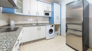 A kitchen with white cabinets, a stainless steel refrigerator, a microwave, a washing machine, and a granite countertop. - Spain Breaks - 2 bed apt With 2 Pools, Airco, Wifi (Benalmádena)