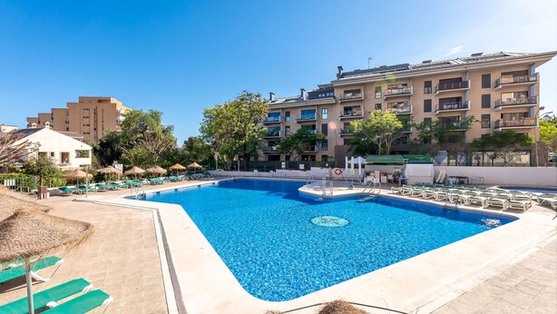 A swimming pool with lounge chairs, a lifeguard stand, and a building with balconies in the background. - Spain Breaks - 2 bed apt With 2 Pools, Airco, Wifi (Benalmádena)